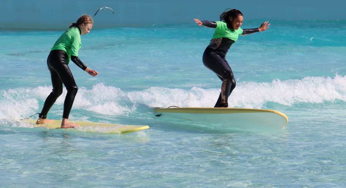 Two young girls in surfing a wave wearing wetsuits and big smiles on their face