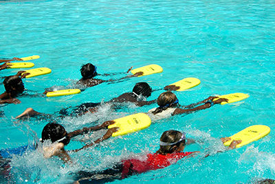Children swimming in a pool holding kick boards out in front