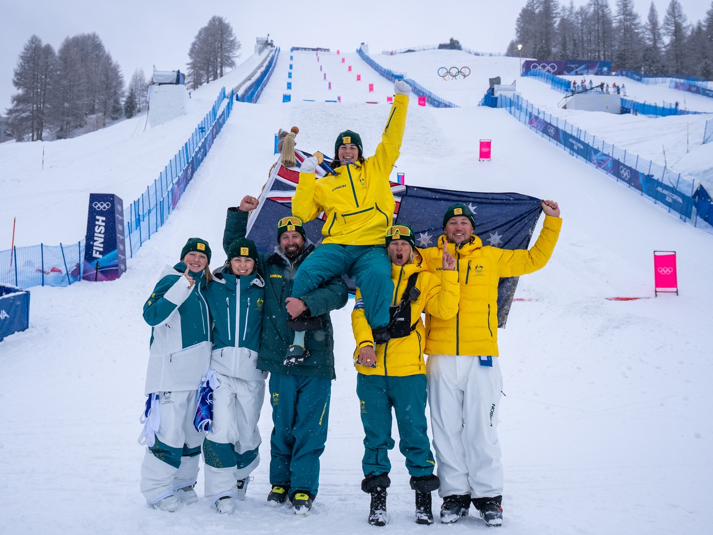Jakara Anthony celebrates winning gold at 2026 Winter Olympic Games with the Australian moguls team, including Gen 32 coach Ethan Topalovic.