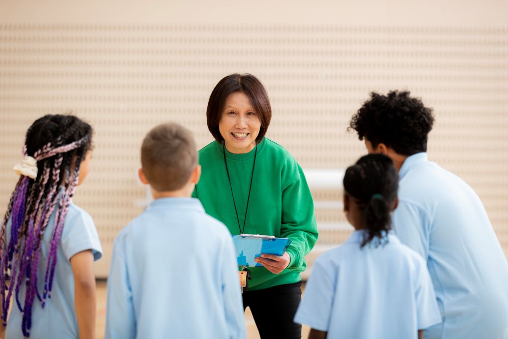 A woman coaching primary aged kids in a gymnasium.