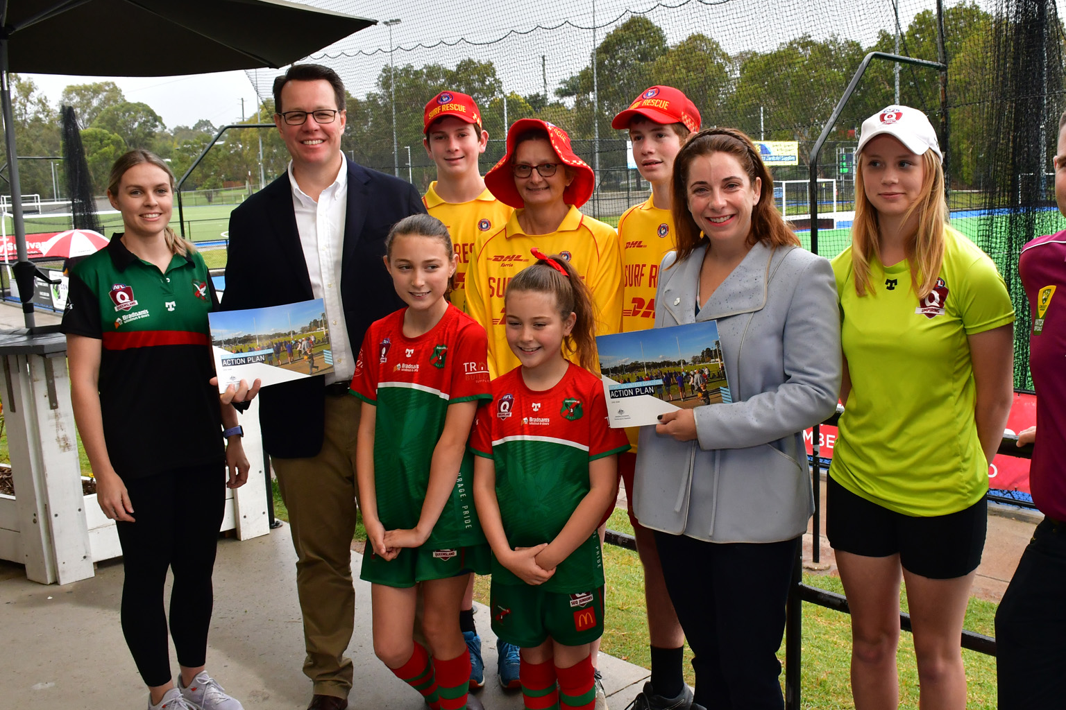 A group of AFL, cricket and surf lifesaving volunteers stand with Kieren Perkins and Anika Wells who hold copies of the Sport Volunteer Coalition Action Plan.