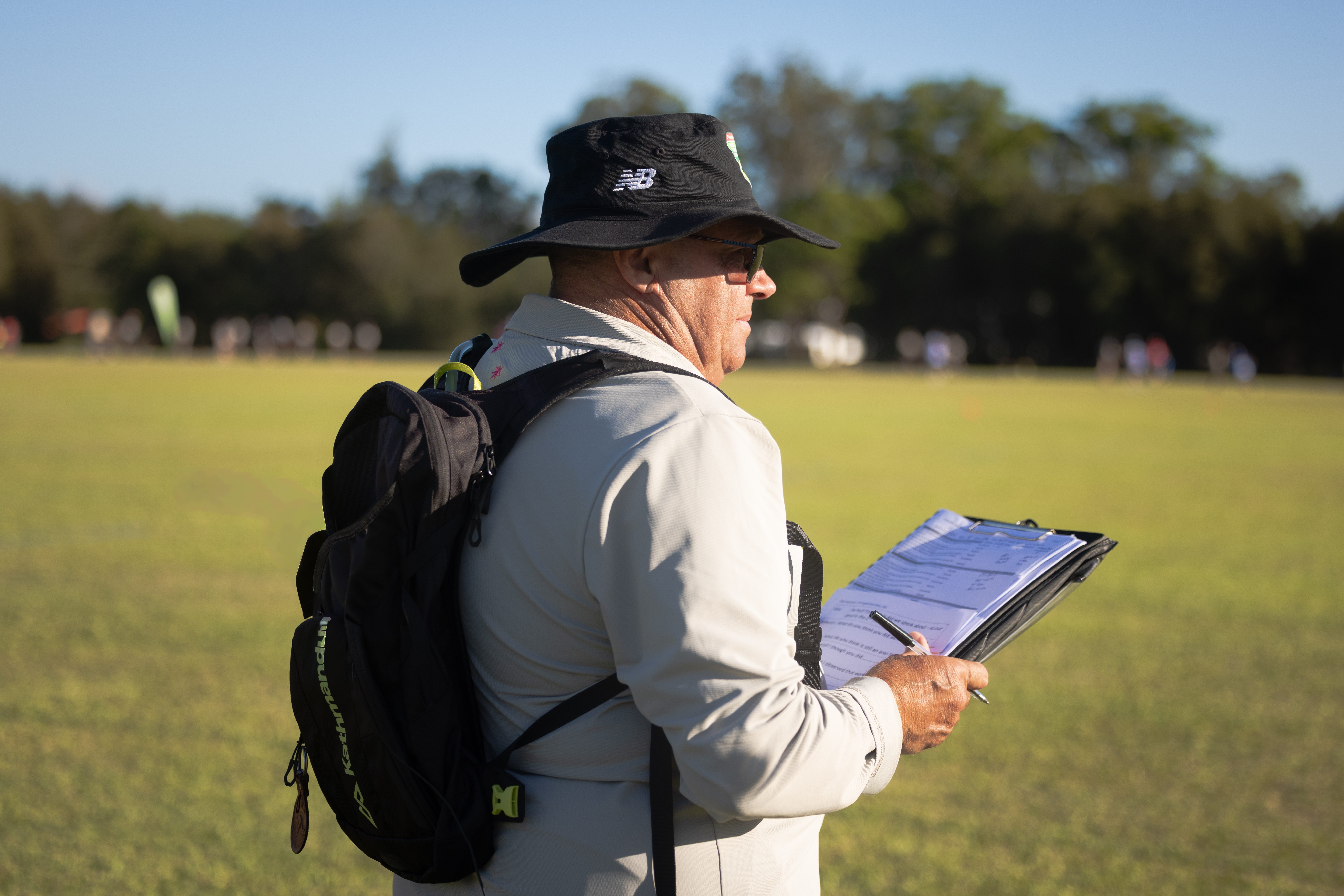 A touch football referee coach observes holding a clip board and pen