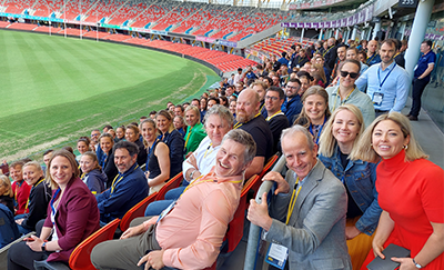 All the participants sitting in the stadium with the oval in the background
