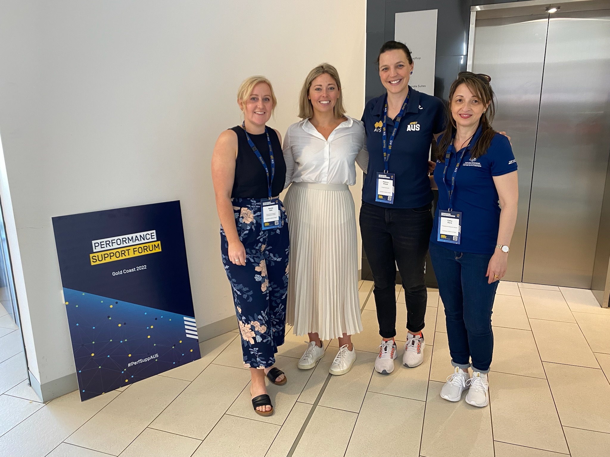 Four females pose in front of the Performance Support Forum sign