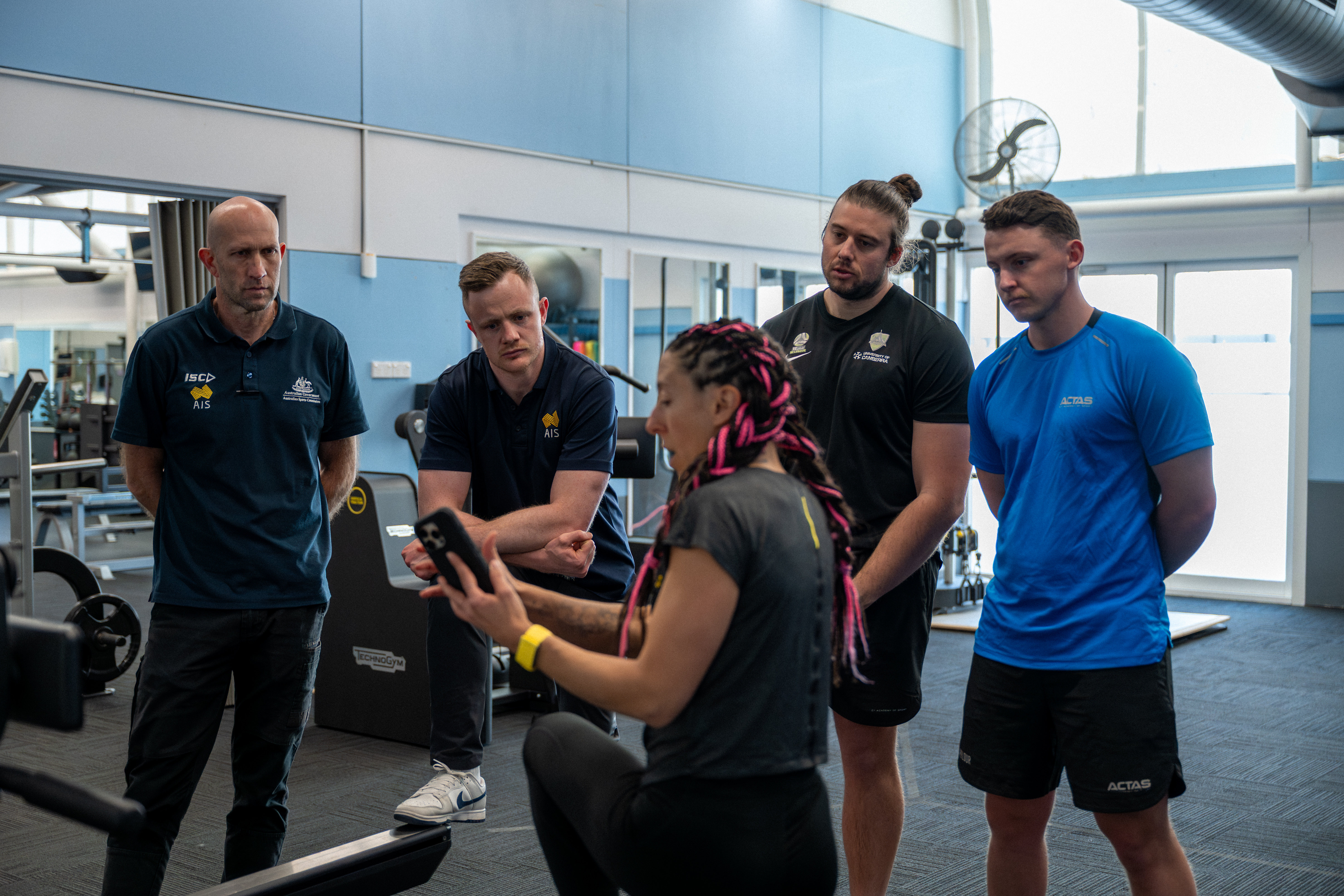 ASC staff look at a display of the live feedback Technogym's equipment provides on a phone held by a staff member demonstrating the equipment