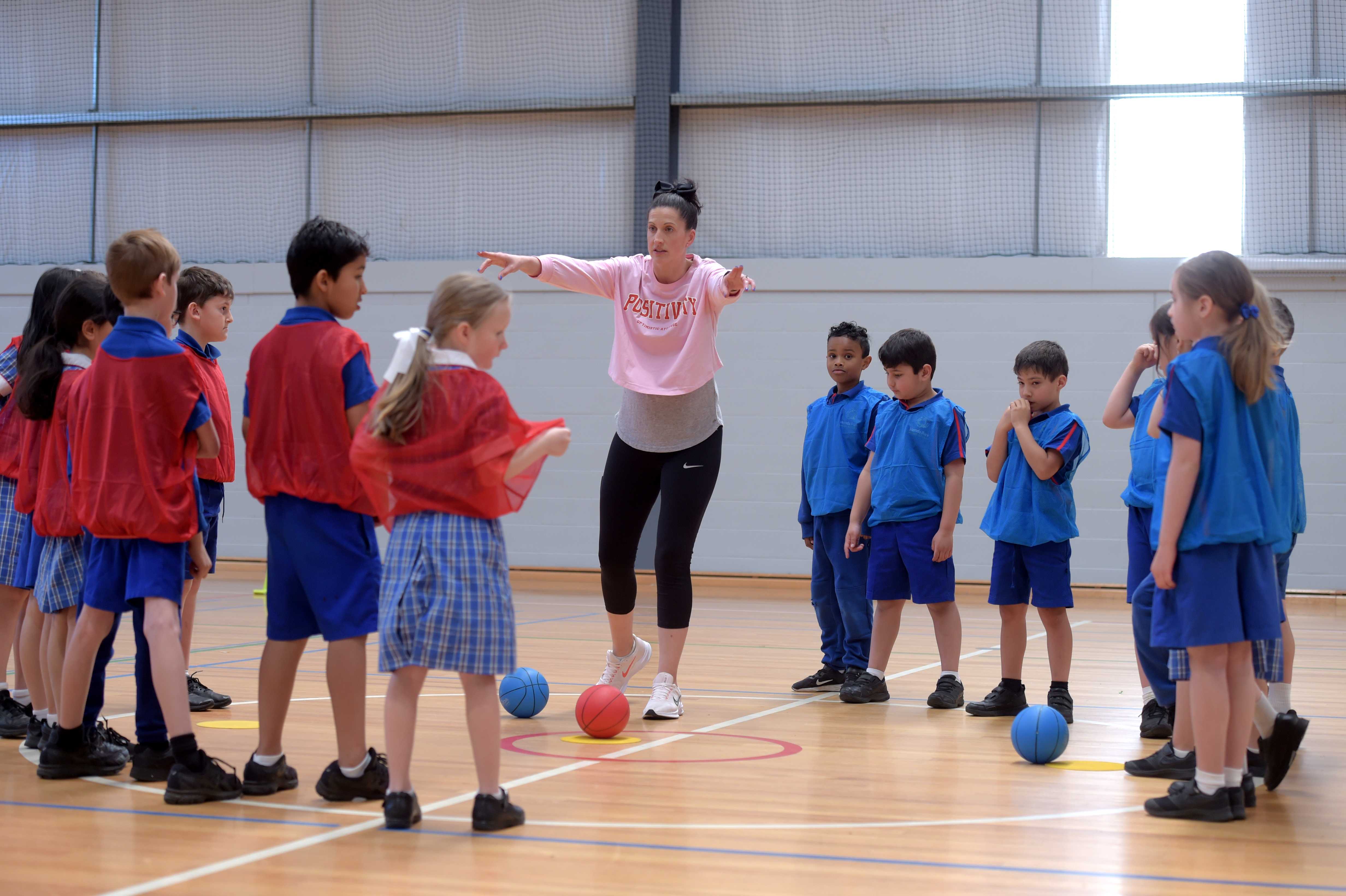 A teacher is on an indoor basketball court with around 12 students who are separated into two teams with a ball.