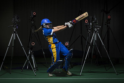 A female athlete swinging a cricket bat in front of motion capture equipment