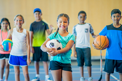A group of children holding an assortment of sports equipment and balls