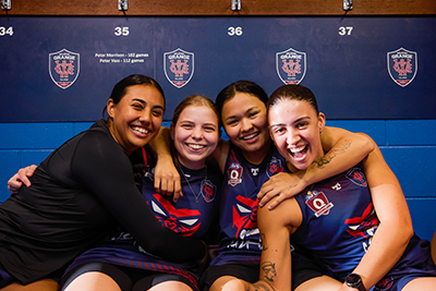 Four girls seated in the change rooms with arms around each other.