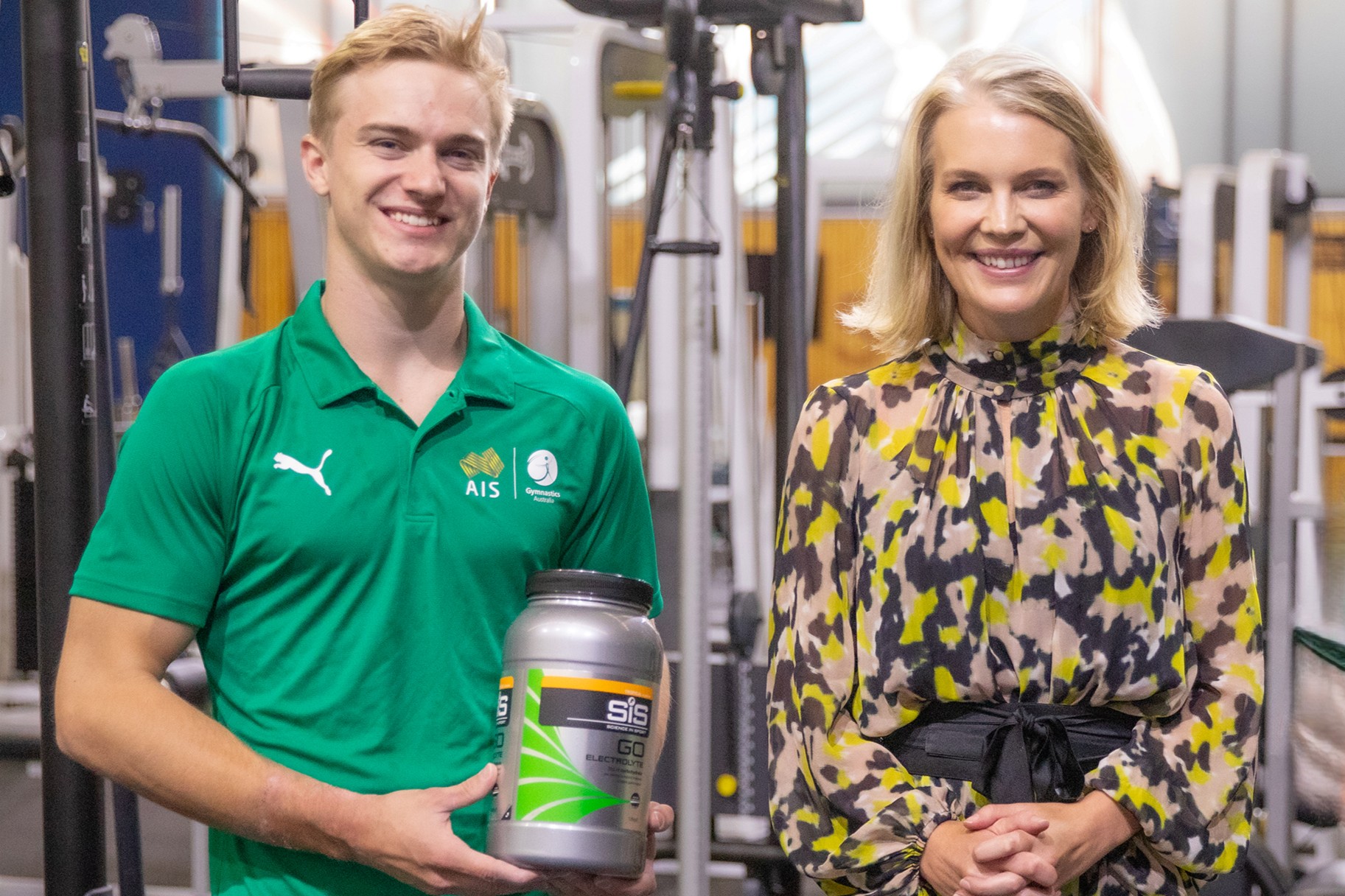 Australian gymnast Blair Stewart is standing next to Executive General Manager of AIS Performance Matti Clements in the AIS gym holding a Science in Sport product.