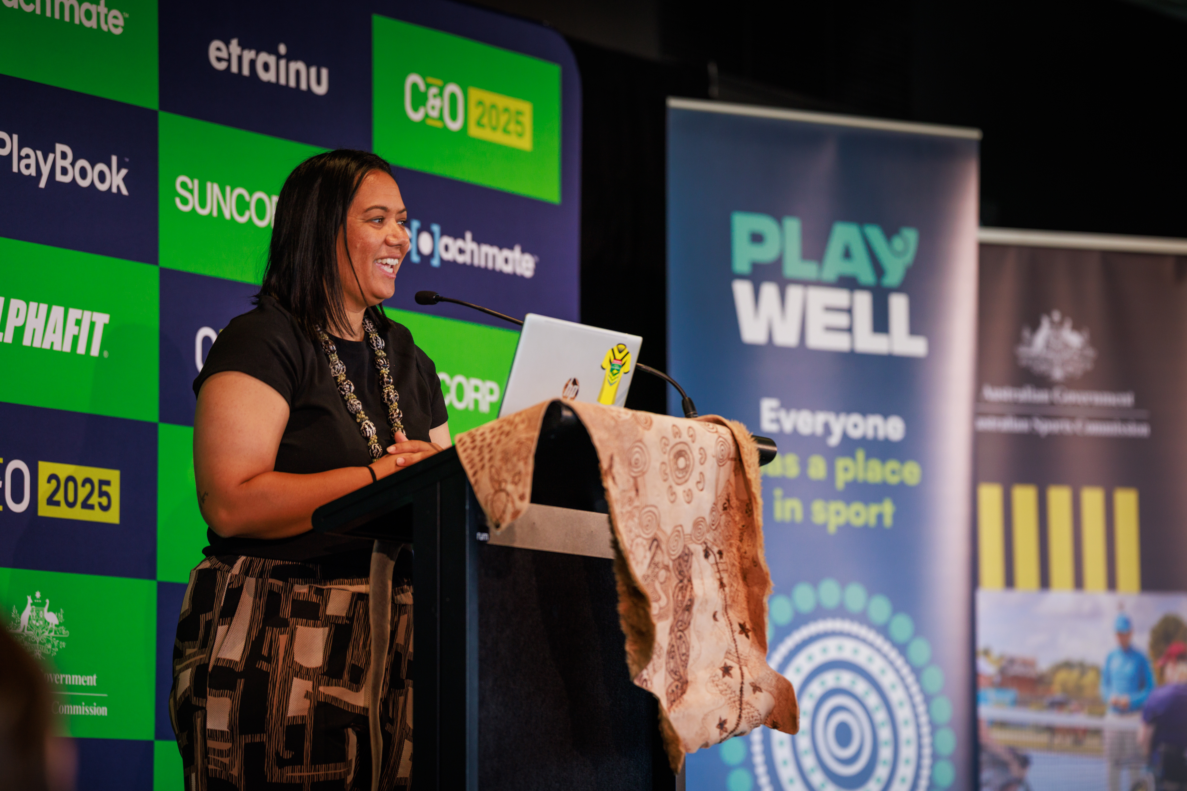 Barkindji (Aboriginal) and Ngāpuhi and Ngāti Hine (Māori) woman and NRL coach Jess Skinner stands at a podium while she addresses the Coaching and Officiating conference on connection to place.