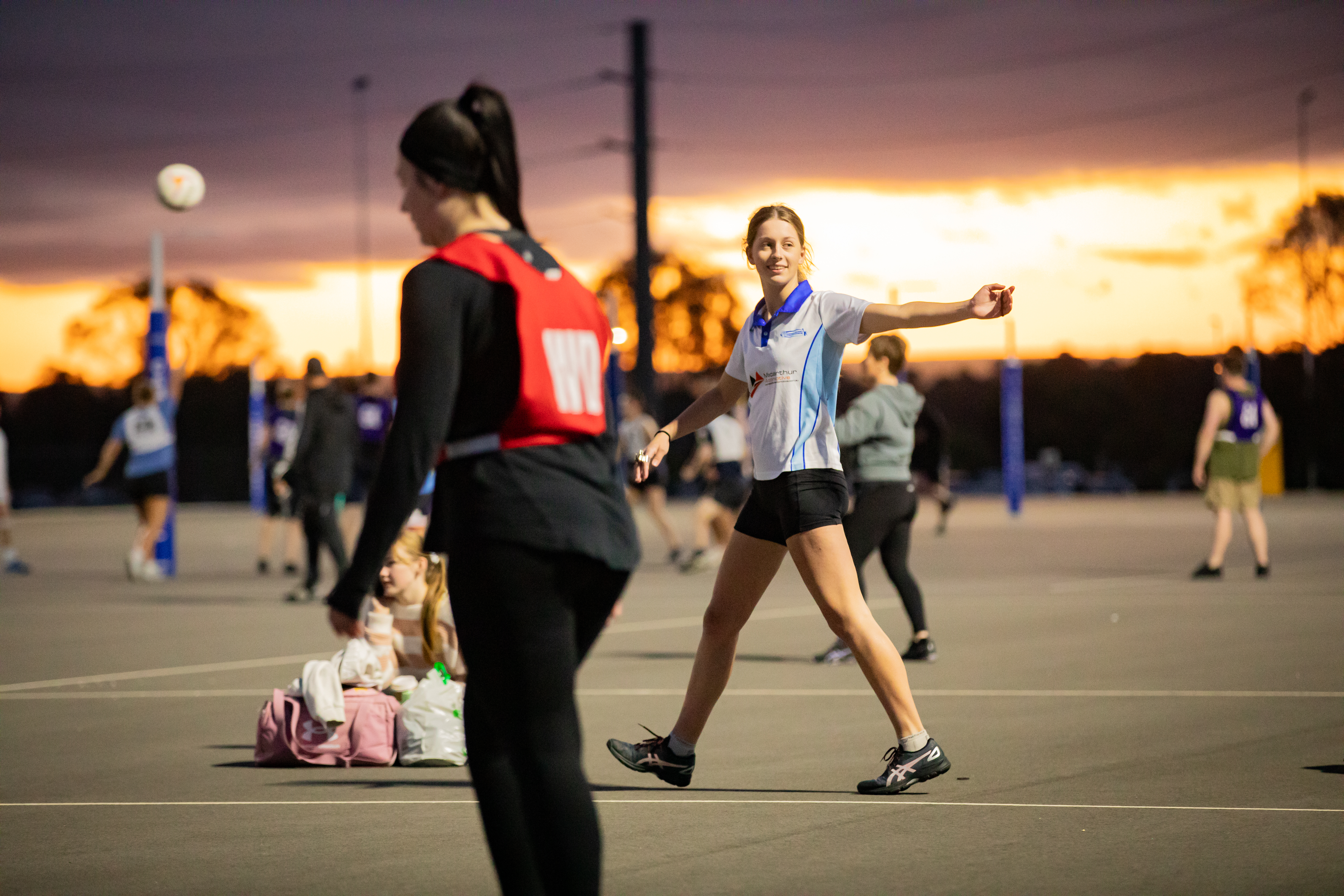 Image of a female netball umpire giving directions to players on a court as the sun sets in the background
