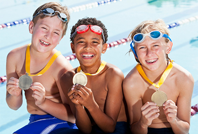 Three young boys smiling holding their swimming medals