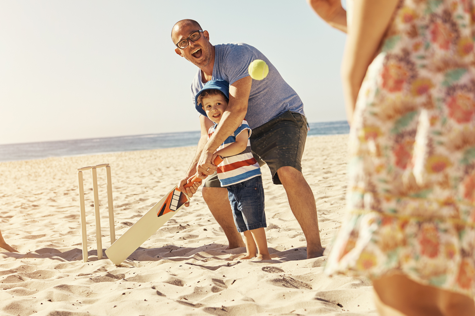 Father and child play beach cricket