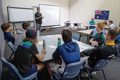 Athletes sitting and listening to an expert talk in a classroom setting