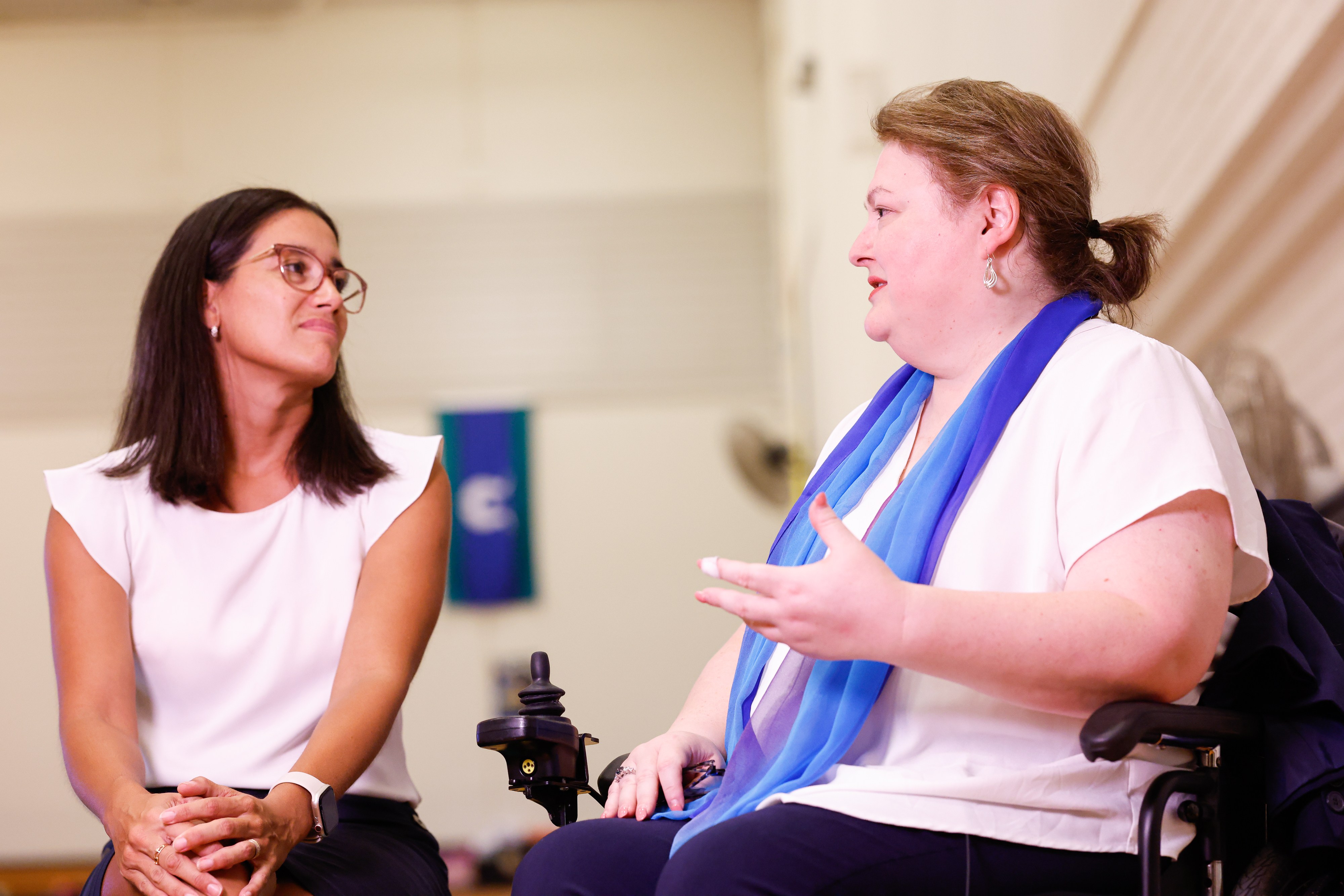 A gymnastics judge seated in a wheelchair on the right talks with a gymnastics judge on the left